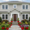 GoHooked 10-inch red plastic planters with vibrant flowers and greenery line a stone pathway leading to a home.