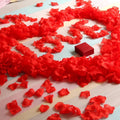 GoHooked red artificial rose petals scattered on a striped surface with a small red gift box.