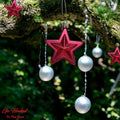 Go Hooked red star and silver ball Christmas ornaments hanging from a mossy tree branch. Festive, reusable decor.