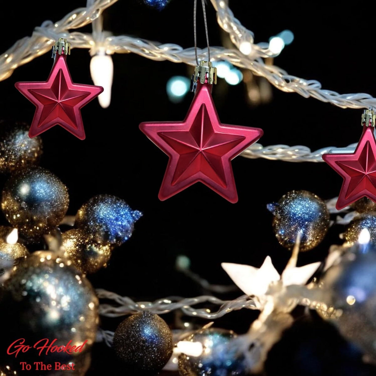Go Hooked red star ornaments with glitter accents, part of a festive Christmas tree decor with blue and gold baubles and fairy lights.