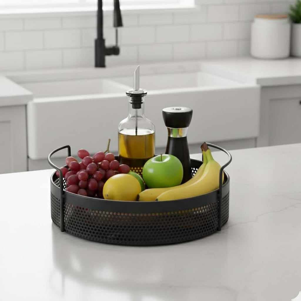 GoHooked round black metal storage tray with perforated design and side handles holding fruit on a kitchen counter
