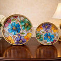 Go Hooked set of 2 round metal decorative trays with colorful floral stained glass art and gold trim.