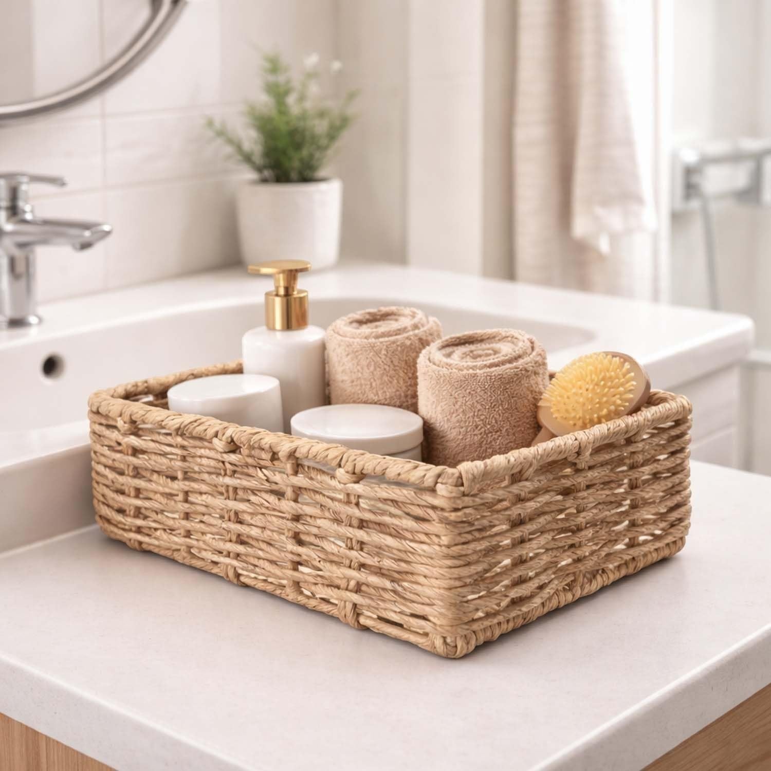 GoHooked handwoven water hyacinth seagrass rectangular basket with handles, holding toiletries and towels on a bathroom counter.