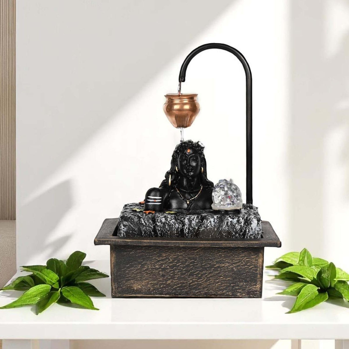 Go Hooked black polyresin tabletop fountain with a Shiva face, copper pot, and LED light. Features a stone texture base and water flow.