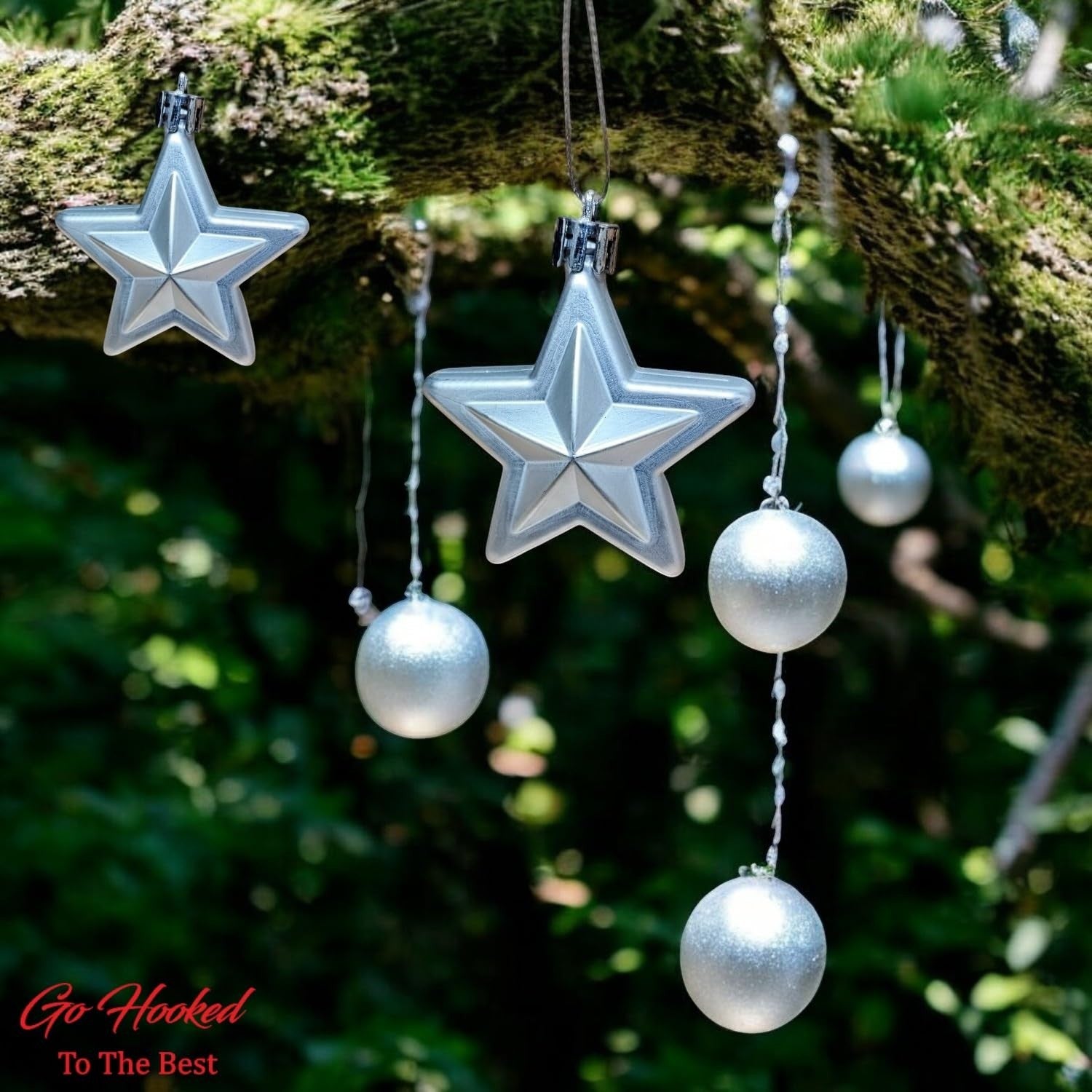 Go Hooked silver star and ball Christmas ornaments with glitter accents, hanging on a mossy branch.