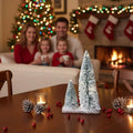 GoHooked snow-flocked mini Christmas trees with warm LED lights on a wooden base, set on a table with pinecones and cranberries.