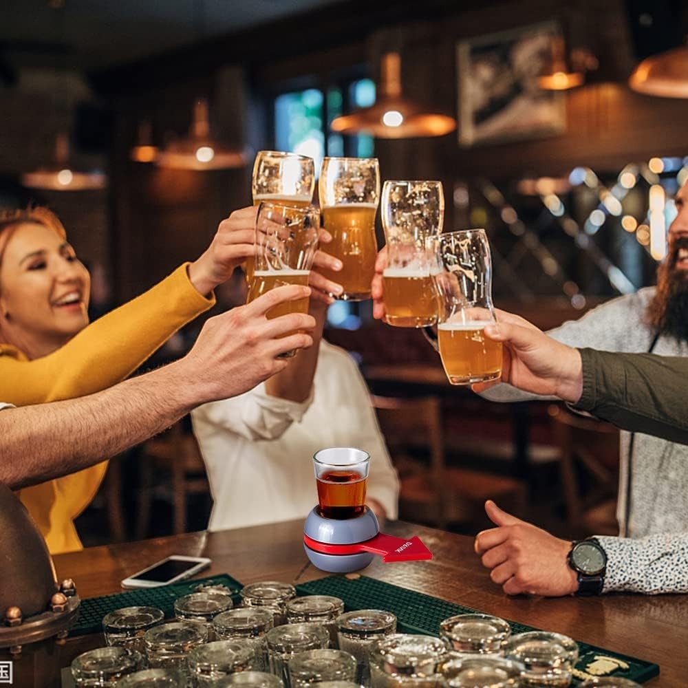 GoHooked Spin the Shot drinking game with a shot glass and spinner on a bar, friends toasting in background.