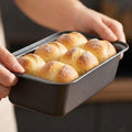 GoHooked grey carbon steel square baking pan filled with six golden brown dinner rolls.