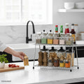 GoHooked stainless steel 2-tier shelf organizer filled with spices, condiments, and pasta. A hand is placing a jar on the shelf.