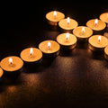 GoHooked tealight candles in matte gold finish holders with flickering flames on a dark textured surface.