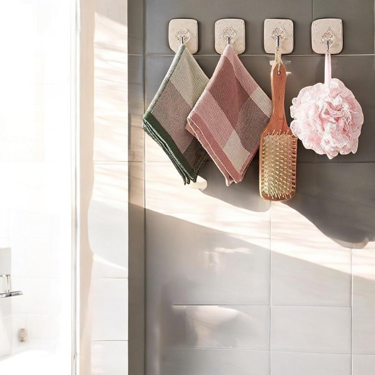 GoHooked transparent adhesive hooks holding towels, a wooden brush, and a pink bath pouf on a tiled wall.