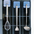 GoHooked transparent adhesive hooks holding kitchen utensils: whisk, pastry brush, and slotted spoon.