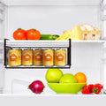 GoHooked black metal under shelf basket organizer holding cans of orange juice in a refrigerator.