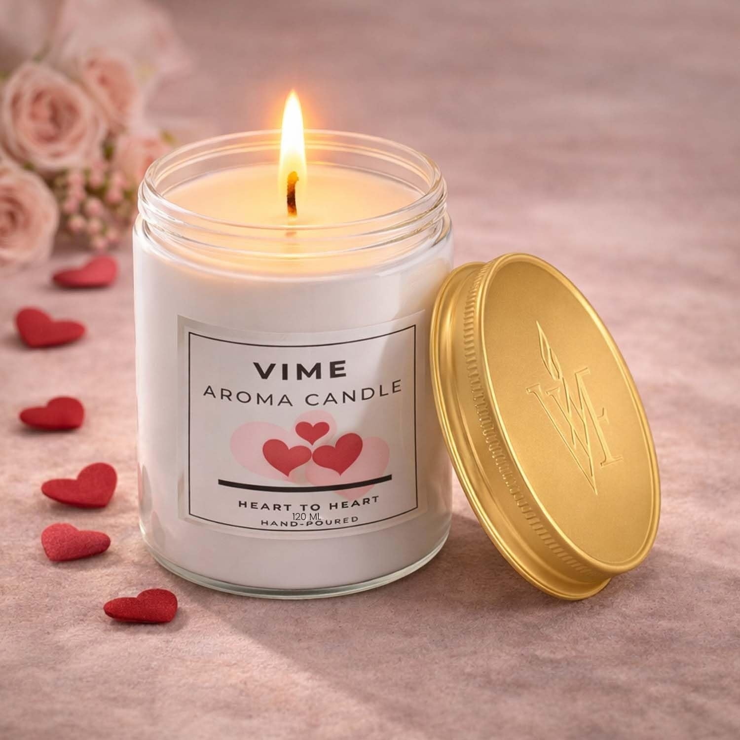 GoHooked ViMe Heart to Heart scented candle in a white glass jar with a gold lid, burning with a warm flame. Decorated with pink hearts.