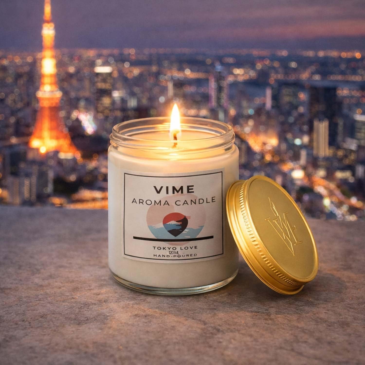 GoHooked ViMe Aroma Candle in Tokyo Love scent, white wax in a glass jar with a gold lid, lit flame.