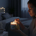GoHooked ViMe white citrus scented candle in glass jar, lit by a woman in a bedroom setting.