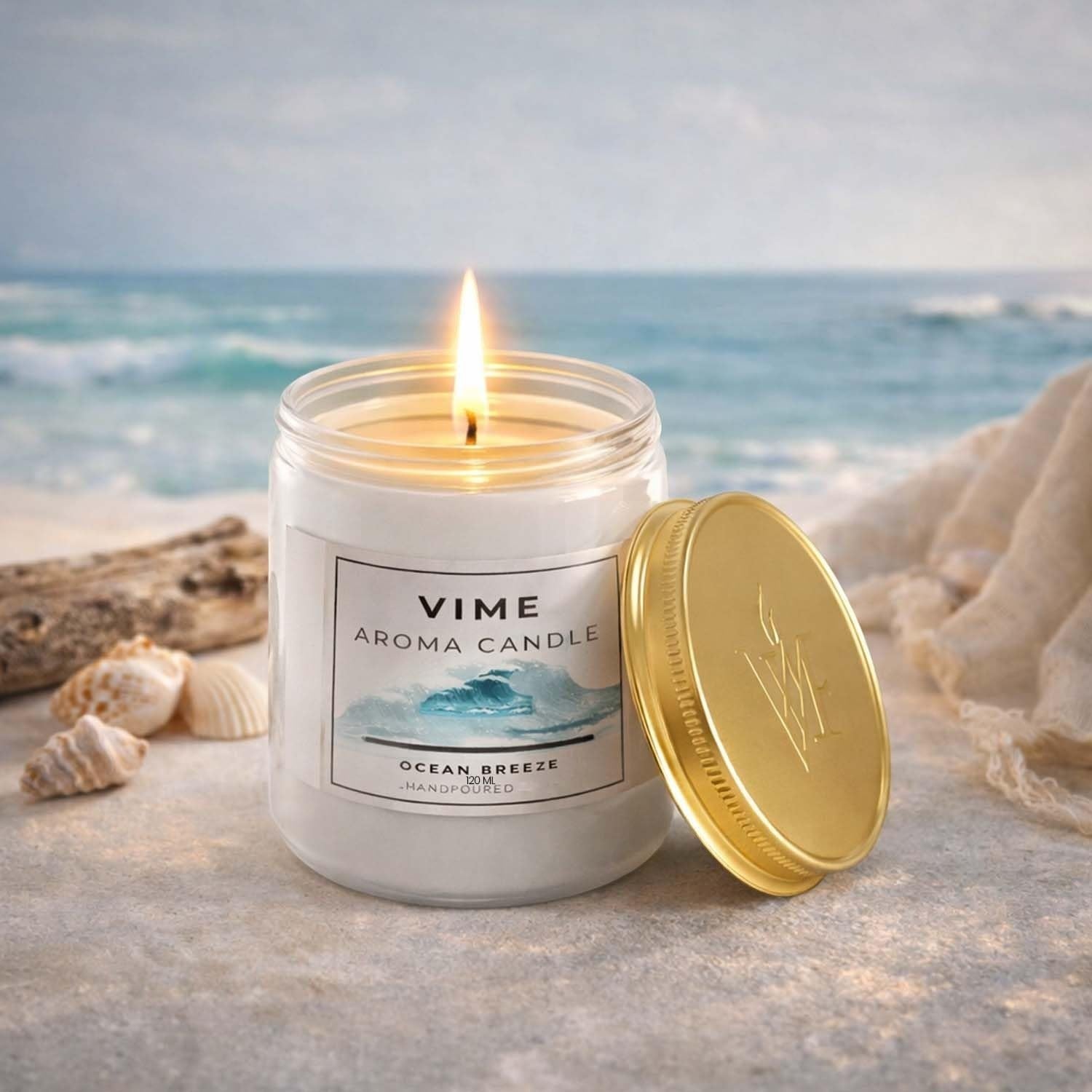 GoHooked ViMe Ocean Breeze aroma candle in a white jar with a gold lid, lit flame, on a beach setting.