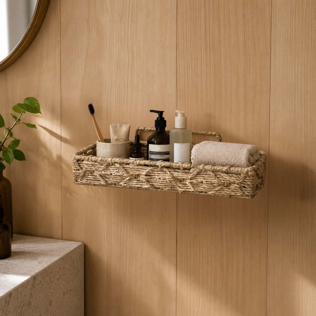 GoHooked wall-mounted handwoven raffia storage basket holding toiletries on a light wood bathroom wall.