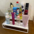 GoHooked white 3-tier metal step rack organizer holding various bathroom and cosmetic products like face wash, lotion, and hairspray.