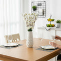 Go Hooked white artificial flowers in a textured white vase on a wooden table with place settings.