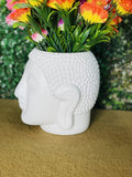 GoHooked white Buddha head shaped plastic planter pot with textured hair detail, holding colorful artificial flowers.