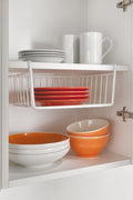 Go Hooked white powder-coated iron under-shelf basket holding orange plates, ideal for kitchen storage.