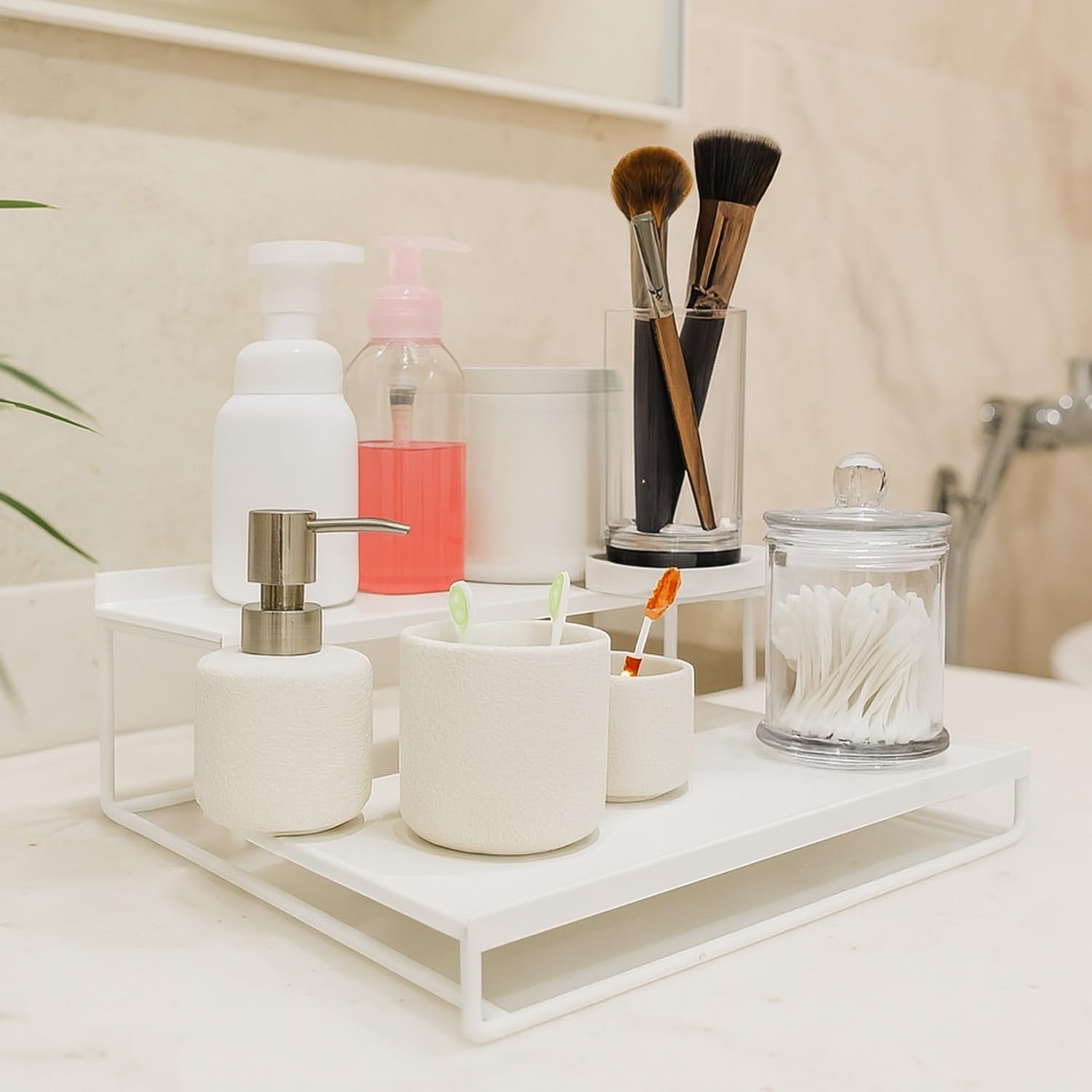 GoHooked 3-tier white metal countertop organizer holding soap dispenser, toothbrushes, makeup brushes, and cotton swabs.