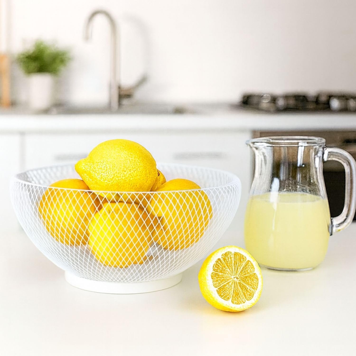 Go Hooked white metal mesh fruit bowl filled with lemons, next to a pitcher of lemonade.