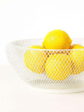 GoHooked white metal mesh fruit bowl filled with fresh yellow lemons on a white background