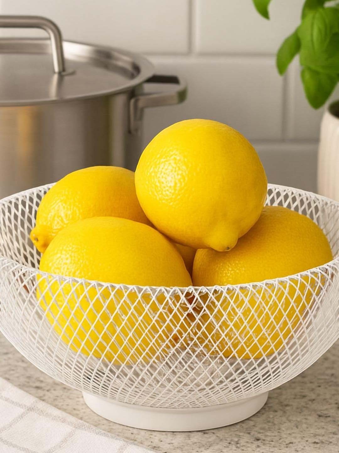 GoHooked white metal mesh fruit bowl filled with fresh yellow lemons on a kitchen countertop