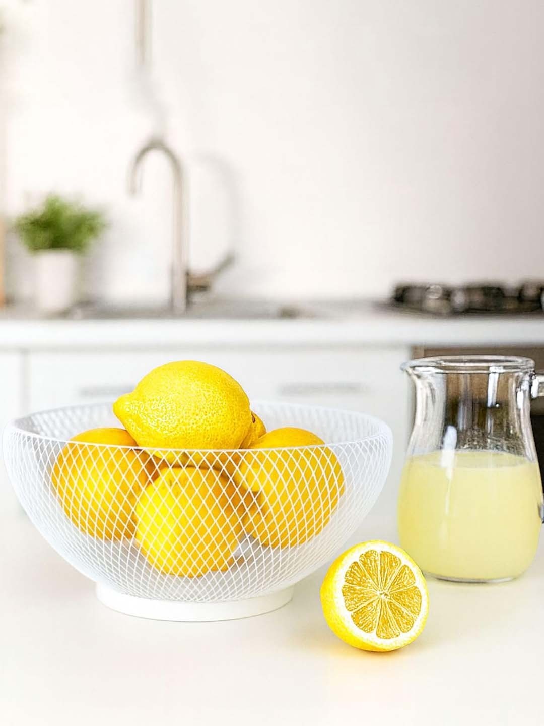 GoHooked white metal mesh fruit bowl filled with fresh yellow lemons on a kitchen countertop