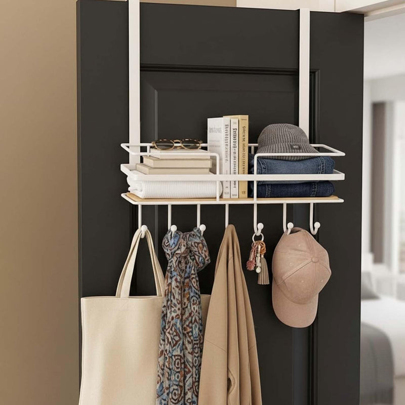 GoHooked white metal over-door organizer with wooden shelf and 5 hooks, holding books, sunglasses, hat, jeans, tote bag, scarf, coat, and keys.