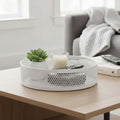 Go Hooked white metal revolving lazy Susan organizer tray with perforated sides, holding a plant, candle, and remotes.