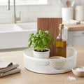 Go Hooked white metal revolving spice rack with honeycomb pattern, holding a potted basil plant and olive oil bottle.