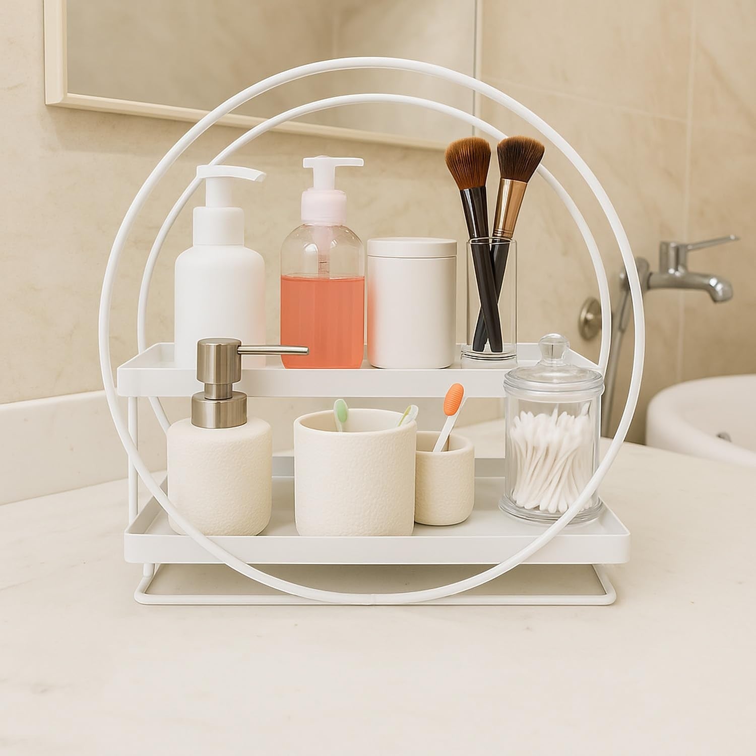 Go Hooked white 2-tier metal vanity organizer with soap dispenser, toiletries, makeup brushes, and cotton swabs.