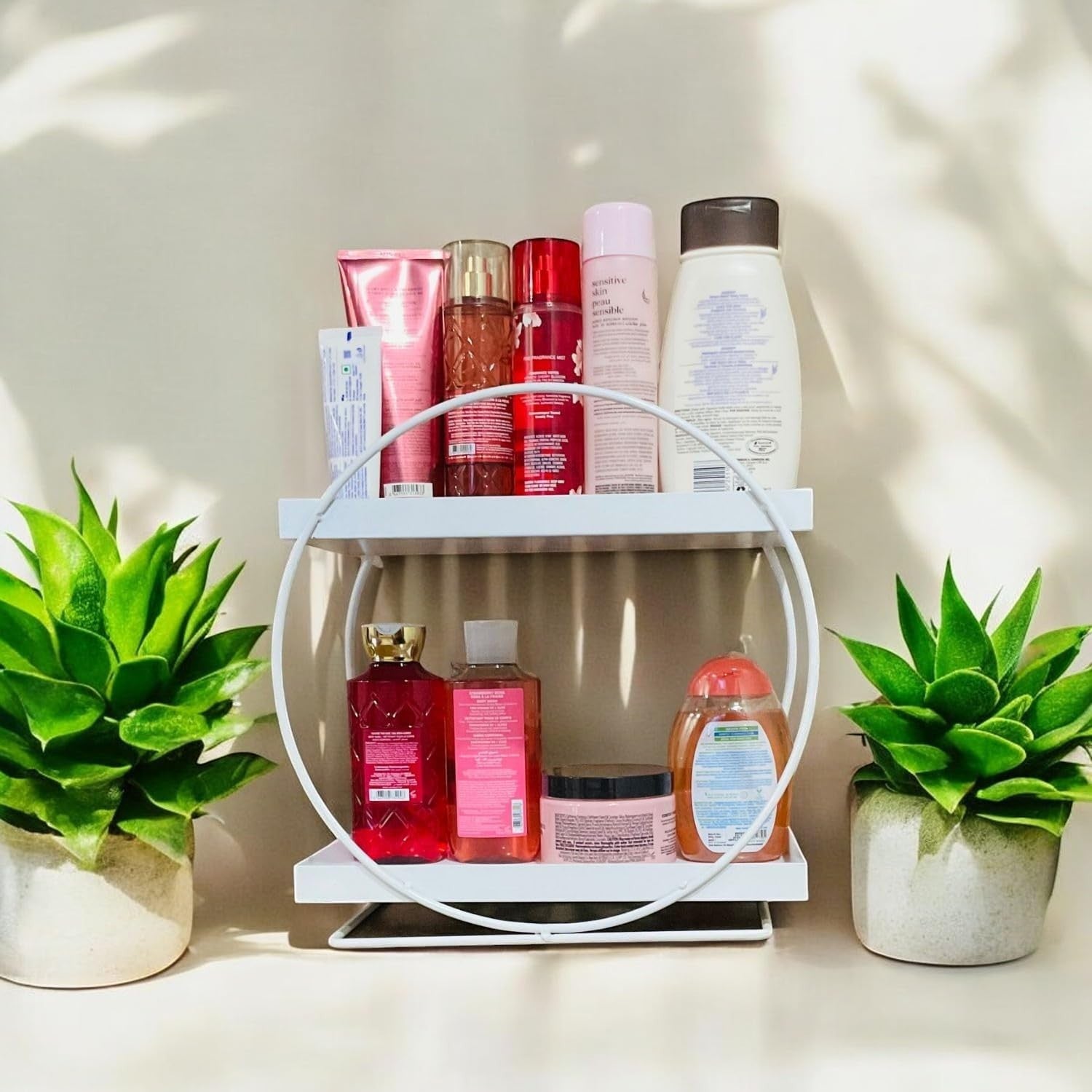 GoHooked white metal 2-tier vanity storage organizer holding toiletries and bath products, flanked by potted plants.