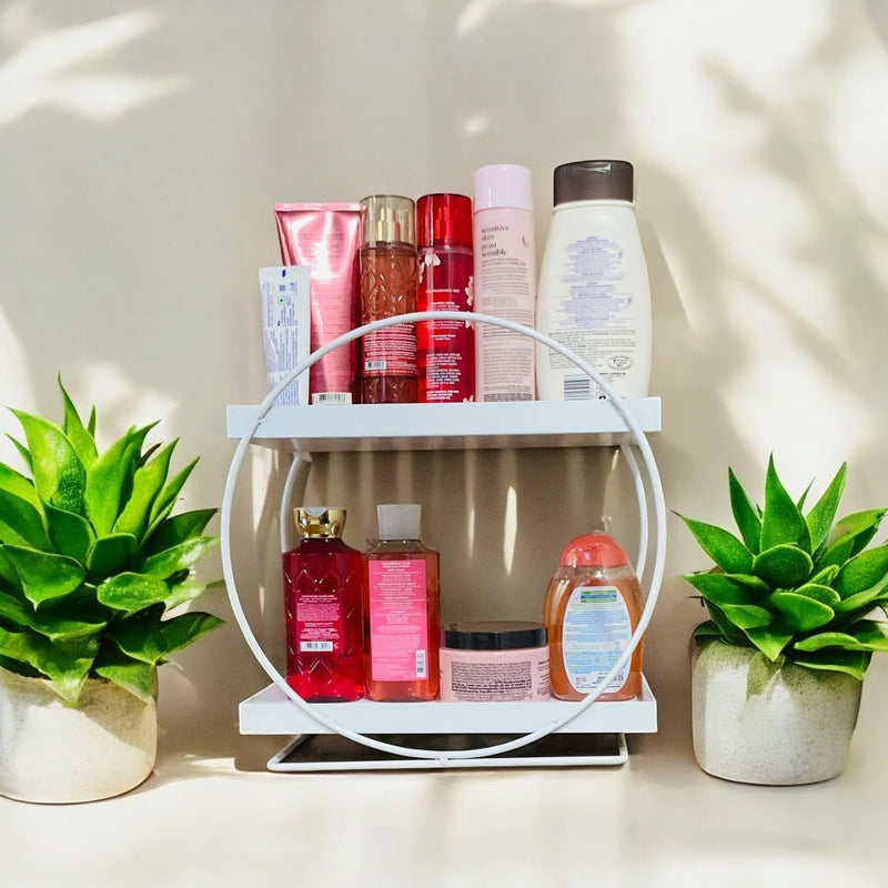 GoHooked white metal 2-tier vanity storage organizer holding toiletries and bath products, flanked by potted plants.