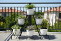 GoHooked white 10-inch plastic flower pots on a tiered black metal stand on a balcony with plants.