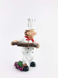 Go Hooked white resin chef figurine holding a wine bottle, with grapes at its base. Eco-friendly design.