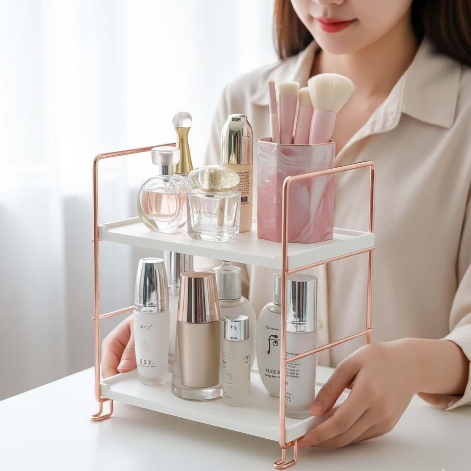 Go Hooked white 2-tier metal and polypropylene shelf rack with rose gold accents, holding skincare and makeup.