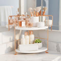 GoHooked white and rose gold 2-tier corner shelf rack holding perfumes, skincare, makeup brushes, and a rolled towel.
