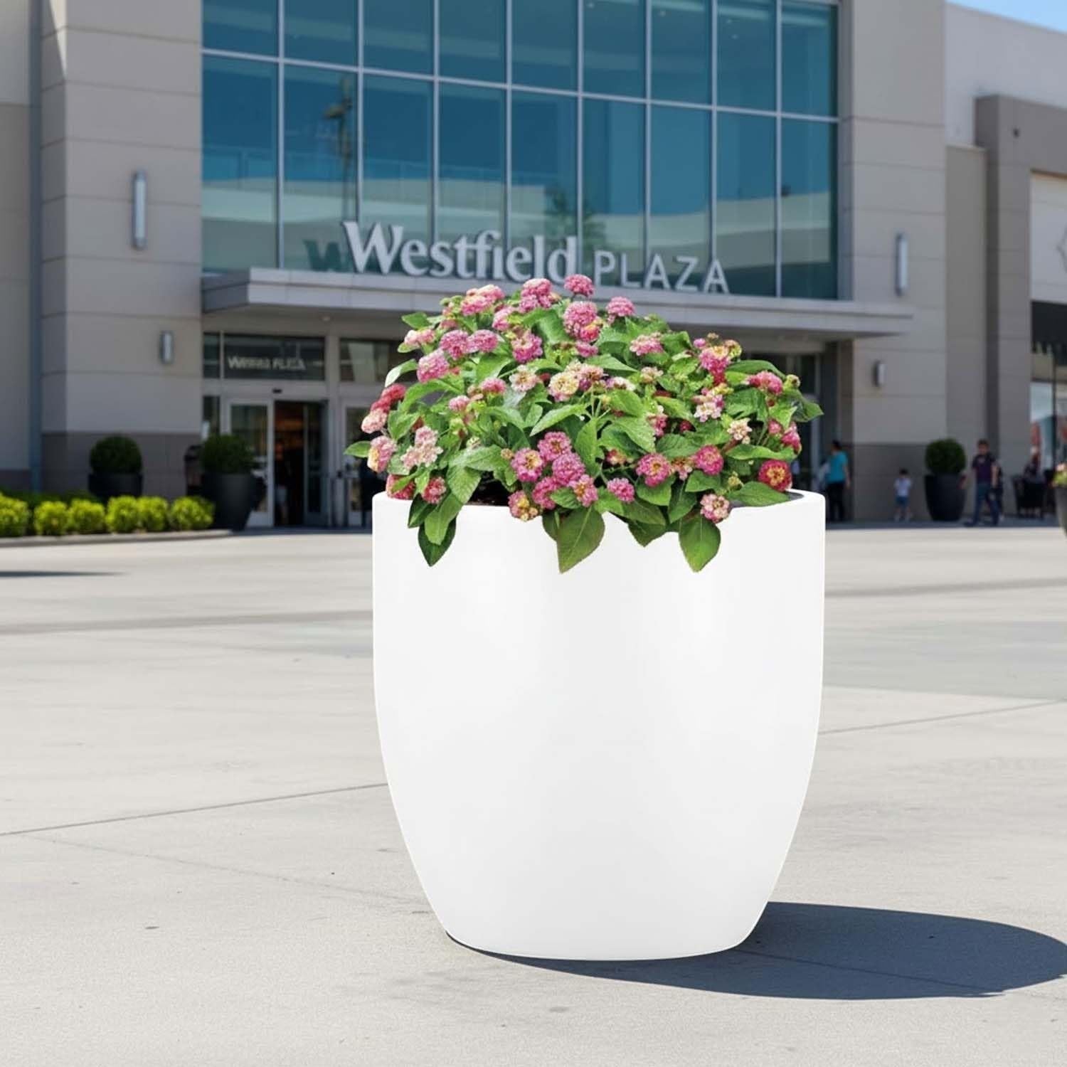 Go Hooked 22-inch modern round white polymer planter with pink flowers, perfect for indoor or outdoor use.