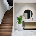 GoHooked white tower planter with a green palm plant in a modern hallway with marble floors and wooden stairs.