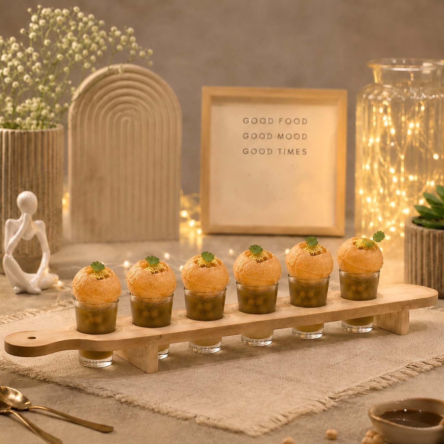 GoHooked wooden serving paddle with six clear shot glasses filled with pani puri, set on a rustic table for entertaining.