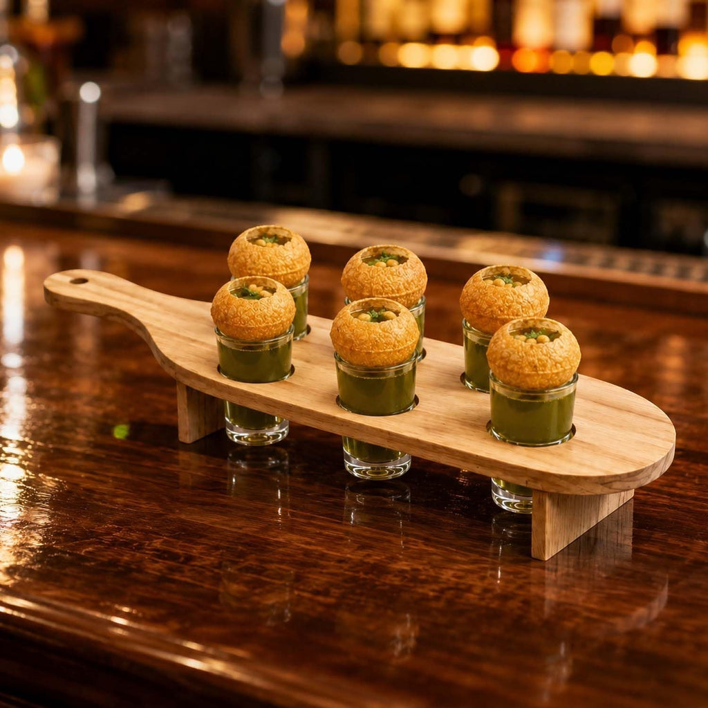 GoHooked wooden serving paddle with six shot glasses filled with green liquid and topped with pani puri snacks