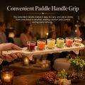 GoHooked wooden shot glass paddle set with six 30ml glasses, held by a hand in a warm, festive party setting.