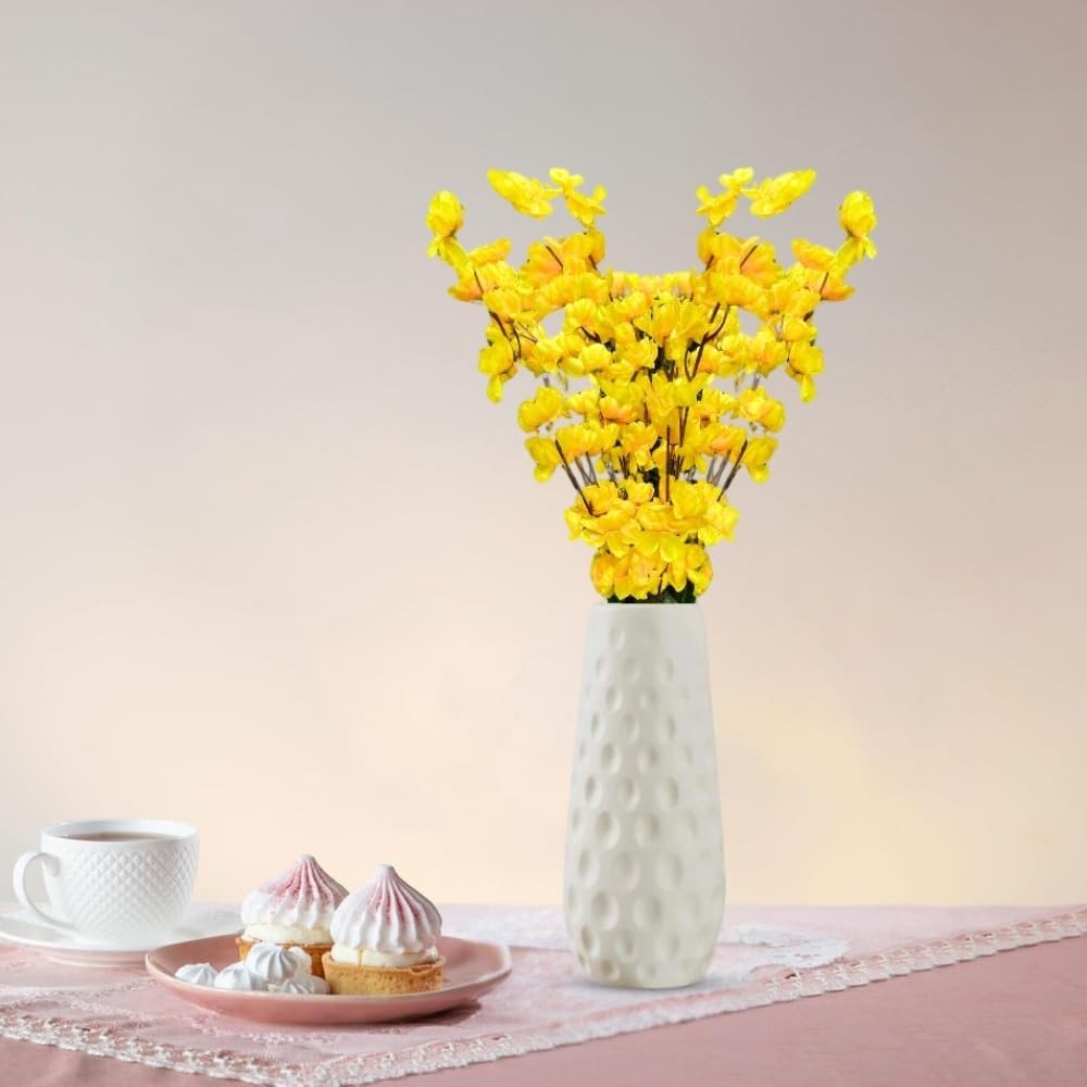 GoHooked yellow artificial flowers in a textured white vase, with pastries and tea on a pink tablecloth.